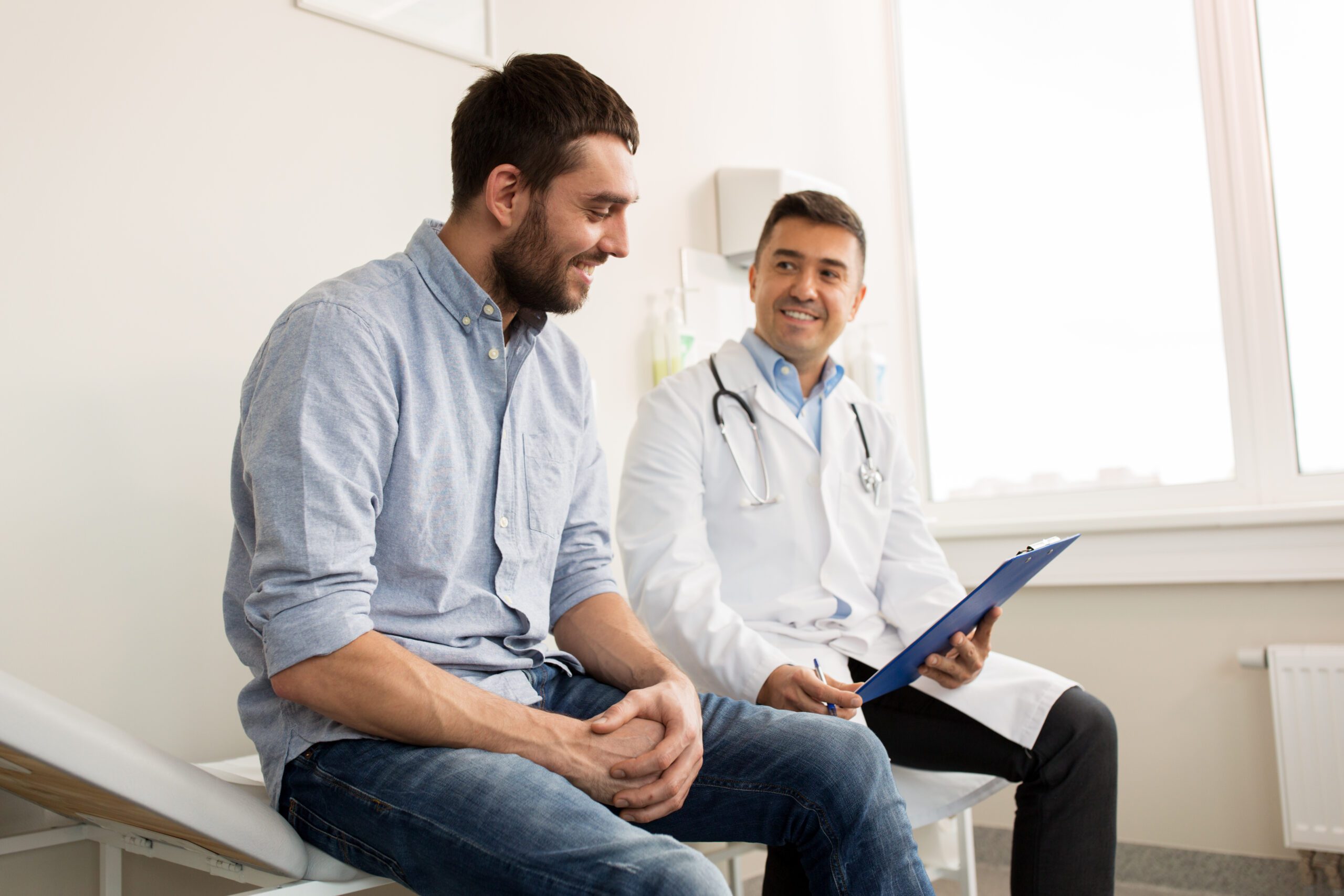 Smiling Doctor With Clipboard and Young Man Patient Meeting at Hospital
